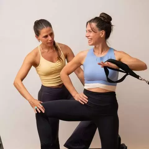 Instructora y alumna sonriendo durante una clase de pilates reformer